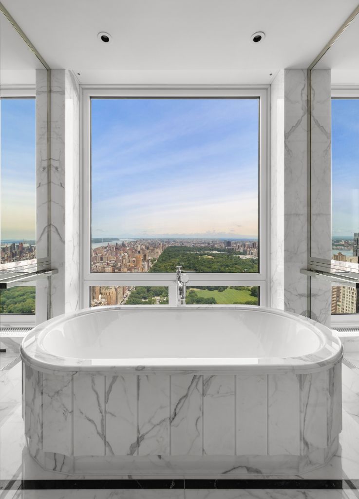 A large white bathtub overlooking the cityscape through a large window in a luxury apartment at 220 Central Park South